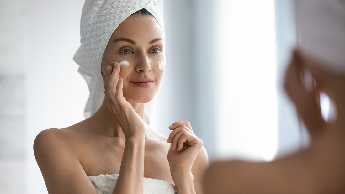 Woman with a towel around her hair applying skincare near her eye